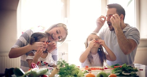 Padres con sus dos hijos jugando con frutas y verduras de la dieta mediterránea