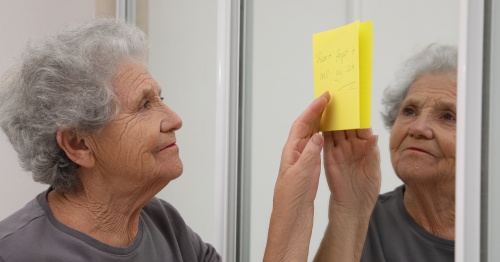 Anciana con deterioro cognitivo leyendo una nota para recordar las tareas