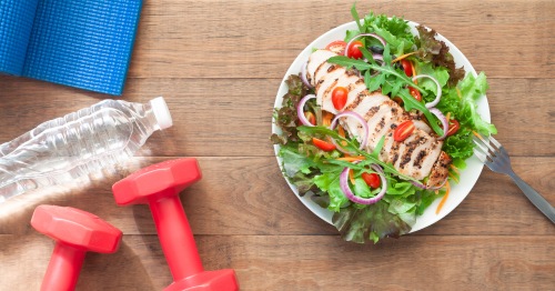 Imagen de una ensalada y unas pesas, representando unos hábitos saludables